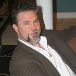 Chris in a white shirt and grey coat.